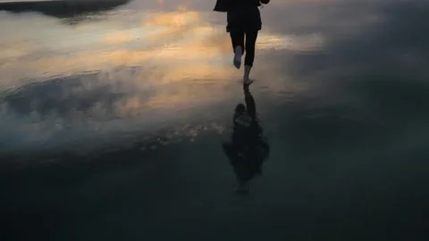 A woman runs on the beach with her reflection at sunset, in New Zealand Stock Footage 215467720