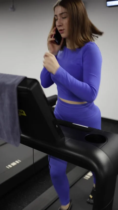 Woman runs on treadmill while talking on smartphone multitasking workout moment Video stock 328253771