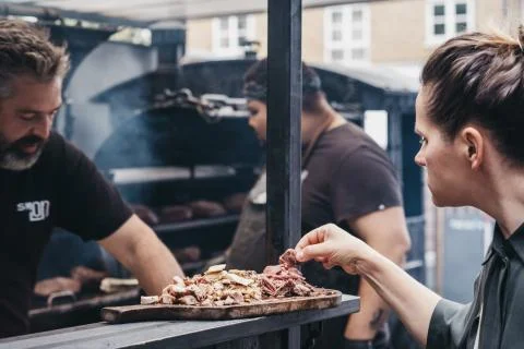 Woman sampling grilled meat at a Smokoloco stall inside Spitalfields Market,  Stock Photos