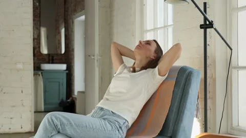 A woman with a satisfied expression sits down in a chair and puts her hands 库存影片 172300718