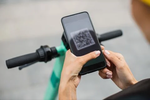 Woman scan QR code by smart phone to unlock and rent electric push scooter on Foto stock