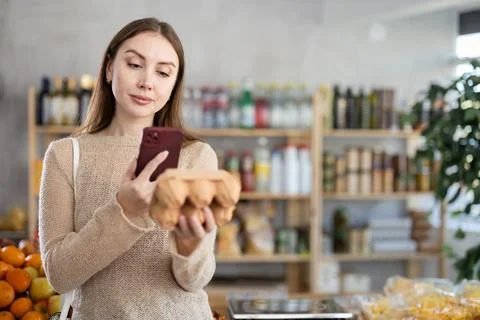 Woman scanning QR code on egg carton during shopping in grocery store Stock Photos