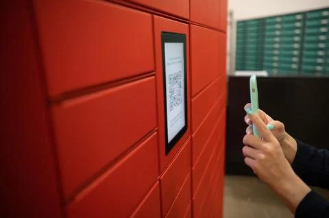 A woman scans a red code to pick up a parcel at a parcel machine. Automated 스톡 사진
