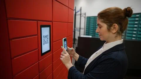 A woman scans a red code to pick up a parcel at a parcel machine. Automated 스톡 사진