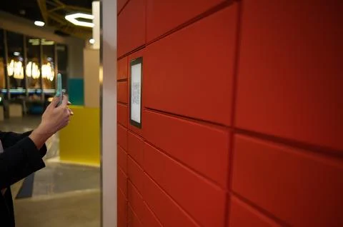 A woman scans a red code to pick up a parcel at a parcel machine. Automated 스톡 사진