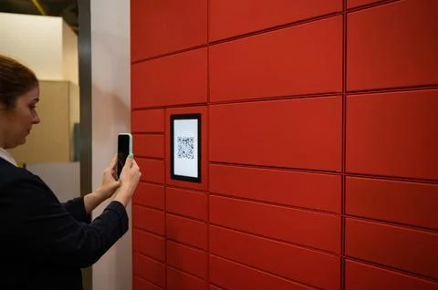 A woman scans a red code to pick up a parcel at a parcel machine. Automated 스톡 사진