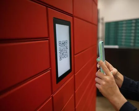 A woman scans a red code to pick up a parcel at a parcel machine. Automated 스톡 사진