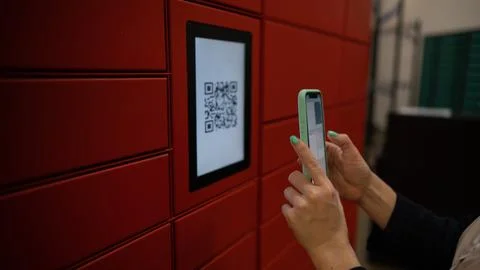 A woman scans a red code to pick up a parcel at a parcel machine. Automated 스톡 사진
