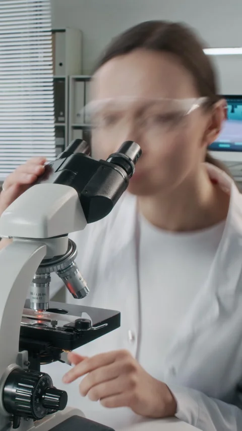 Woman Scientist Looking in Microscope at Desk Time Lapse Vertical Stock Footage 330677177