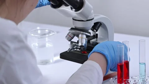 A woman scientist is looking through a microscope eyepiece at a slide with . Video stock 270758386