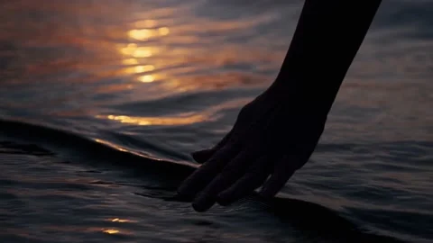 Woman scoops sea water against the sunset. Close-up hand touches the water Stock Footage