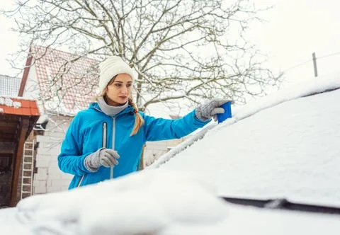 Woman scraping off ice from front window of her car in winter Stock Photos