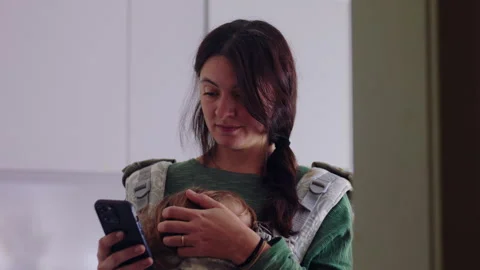 Woman scrolls on her cellphone in the kitchen while stroking her sleeping t.. Stock Footage 343657224