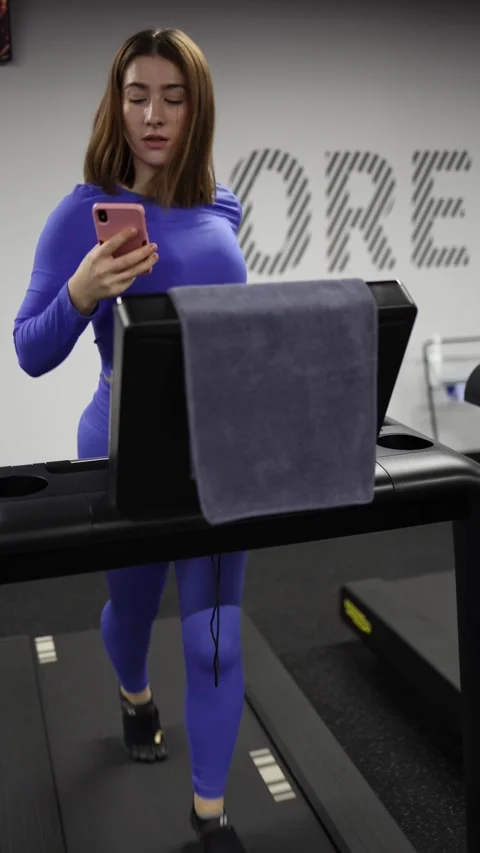 Woman scrolls smartphone while running on treadmill losing focus Stock Footage 328253764