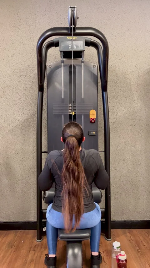 Woman seated lat pulldown rear view long hair - back pull gym training vertical Stock Footage 337380835
