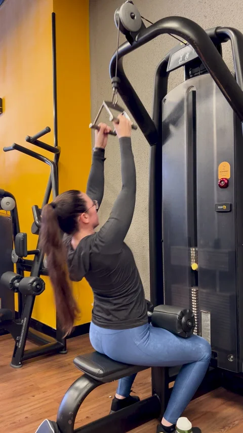 Woman seated lat pulldown triangle bar side view - back training gym vertical Stock Footage 337380641