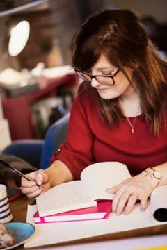 A woman seated at a table making notes, writing in a notebook. Stock Photos