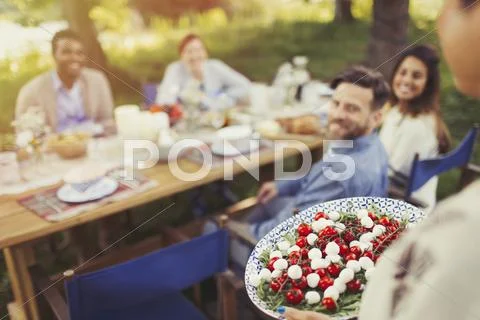 Woman serving Caprese salad appetizer to friends at patio table Stock Photos