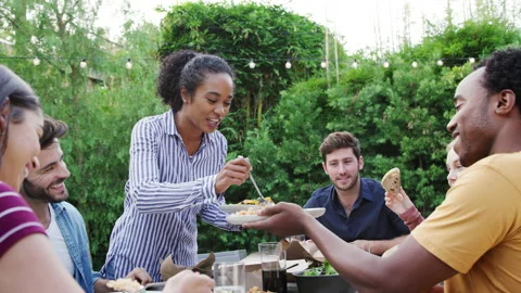 Woman Serving Group Of Multi-Cultural Friends At Home At Table Enjoying Food At Stock Footage