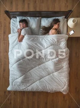 The woman set alarm on the bed near the husband. view from above Stock Photos