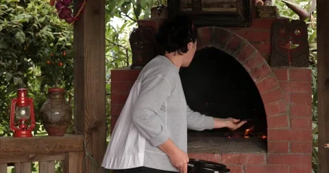 Woman set fire and put cooking clay pot into rustic brick oven outdoors Stock Footage 165198804