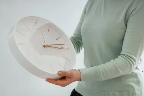 Woman setting time on wall clock on light background. Daylight saving time co Stock Photos
