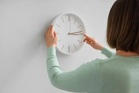 Woman setting time on wall clock at home, back view. Daylight saving time con Stock Photos
