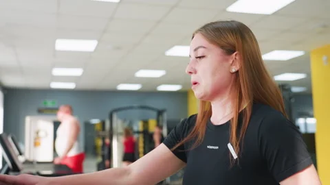 Woman Setting Treadmill Speed While Making Facial Gesture in Modern Gym Stock Footage 308320634