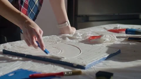 Woman shaping textured paste on white canvas using palette knife on work table Video stock 330559429