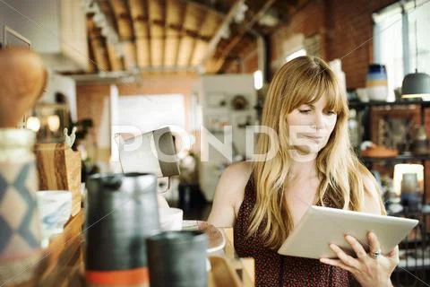 Woman in a shop, holding a digital tablet and ceramic jug. Stock Photos