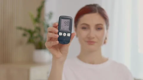 Woman shows glucometer reading of 98 mg dL in home setting Stock Footage 346703896