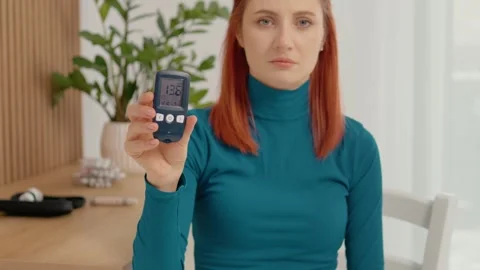 Woman shows glucometer reading indicating high blood sugar level of 136 mg dL Stock Footage 334033932