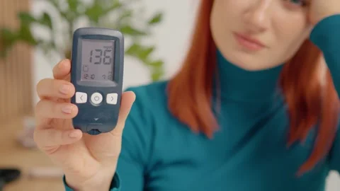 Woman shows high glucometer reading of 136 mg dL in home setting Stock Footage 334034007