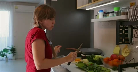 Woman singing with spoon in kitchen, surrounded by fresh vegetables Видео 305936282