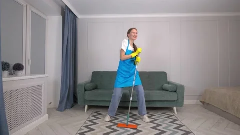 Woman singing while mopping floor in living room, using mop as microphone, Stock Footage 231331147