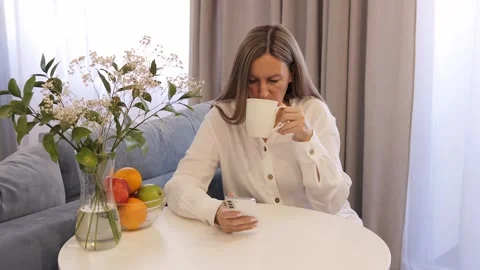 Woman sipping coffee while deeply engrossed in her mobile phone. Female focused Stock Footage 274193100