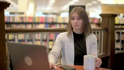 A woman sips coffee while working on her laptop in a bookstore cafe. Surround Stock Footage 275799126