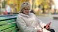 Woman sits on the bench in the city park and communicates via red smartphone HD Footage