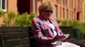 Woman sits on the bench in courtyard and uses white smartphone HD Footage