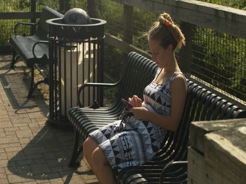 Woman sits on bike path bench with phone Stock Footage 83087553