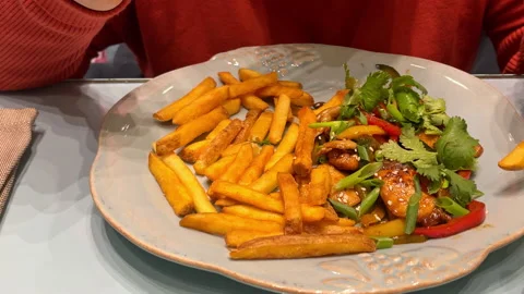 Woman sits in a cafe and eats fries and vegetables with a fork, plate with food Stock Footage 165192986