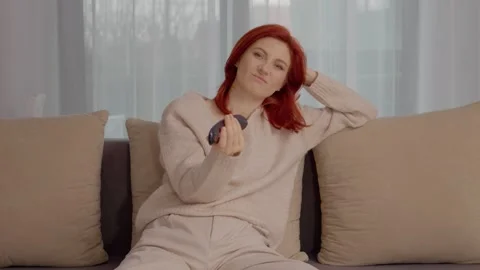 Woman sits on couch and changes TV channels during quiet afternoon Stock Footage 329633891