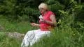 Woman sits on a fallen tree in the forest and listens to music HD Footage