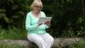Woman sits on a fallen tree in the forest and uses Tablet PC HD Footage