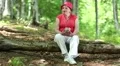 Woman sits on a fallen tree in the forest listens to music and sings a song HD Footage