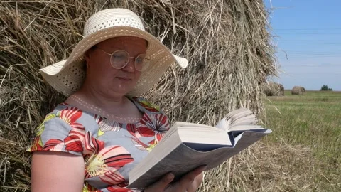 A woman sits in a field next to a haystack and reads a book. Stock Footage 135496777