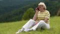 Woman sits on a green grass and talks on a cell phone HD Footage