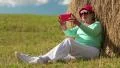 Woman sits on green grass near haystack and makes photos on his smartphone HD Footage
