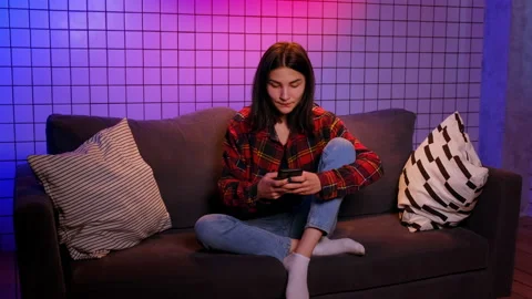 Woman sits on sofa texting message to friend on smartphone Stock-Footage 201423746