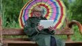 Woman sits on swing bench with multicolor umbrella in green raincoat HD Footage